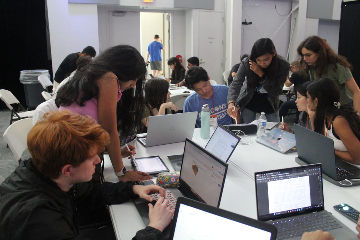 Students gathered around laptops and tablets working on a design together
